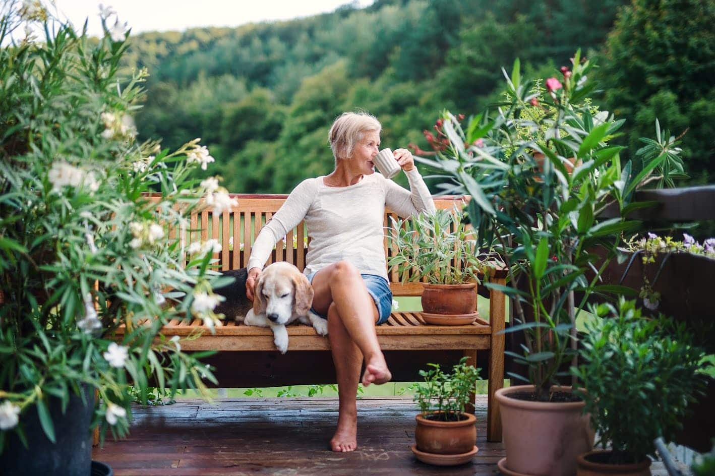 Older woman enjoying coffee on the patio bench with her dog.